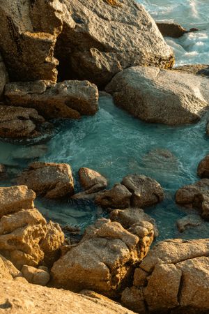 Turquoise water flowing between golden coastal rocks during sunset.
