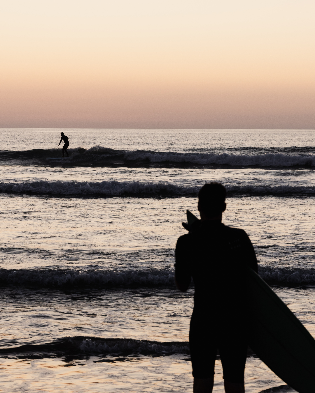 Silhouette of a surfer watching waves at sunset.