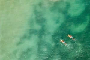 Aerial view of two surfers floating in clear turquoise ocean water.