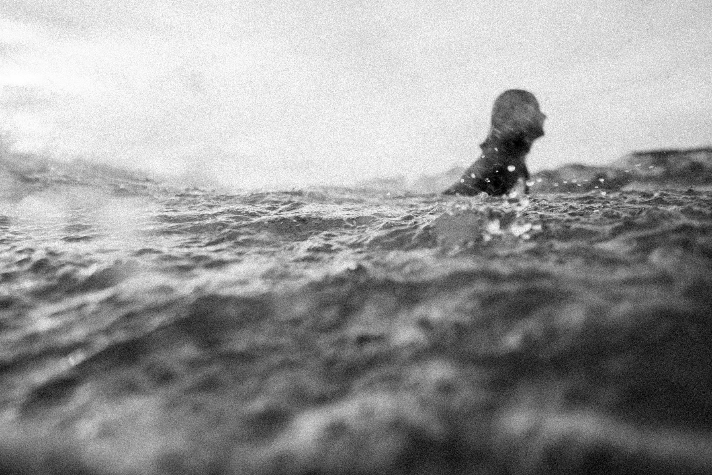 Black and white photo of someone swimming in choppy ocean water.