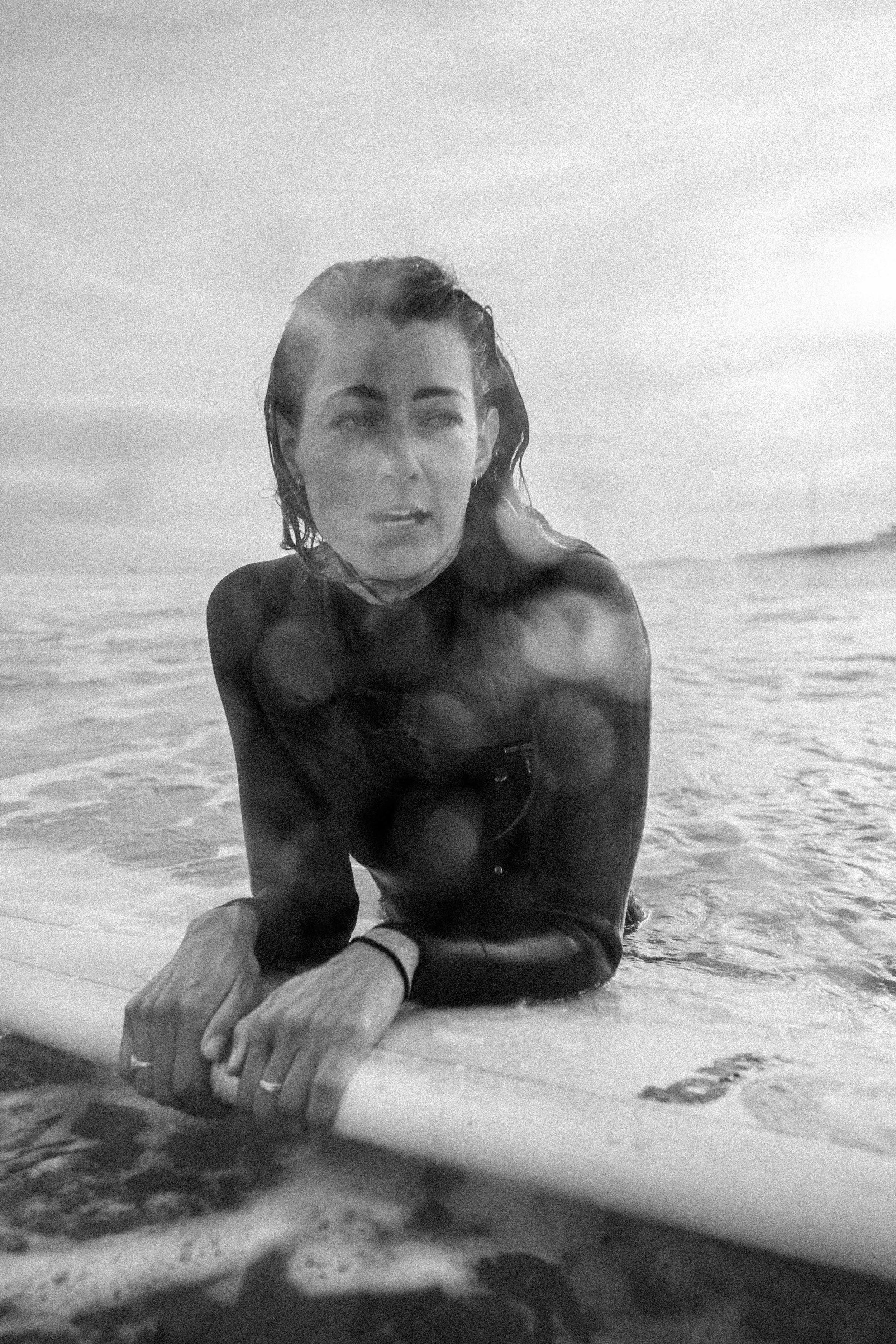 Surfer in wetsuit lying on surfboard in ocean waves.