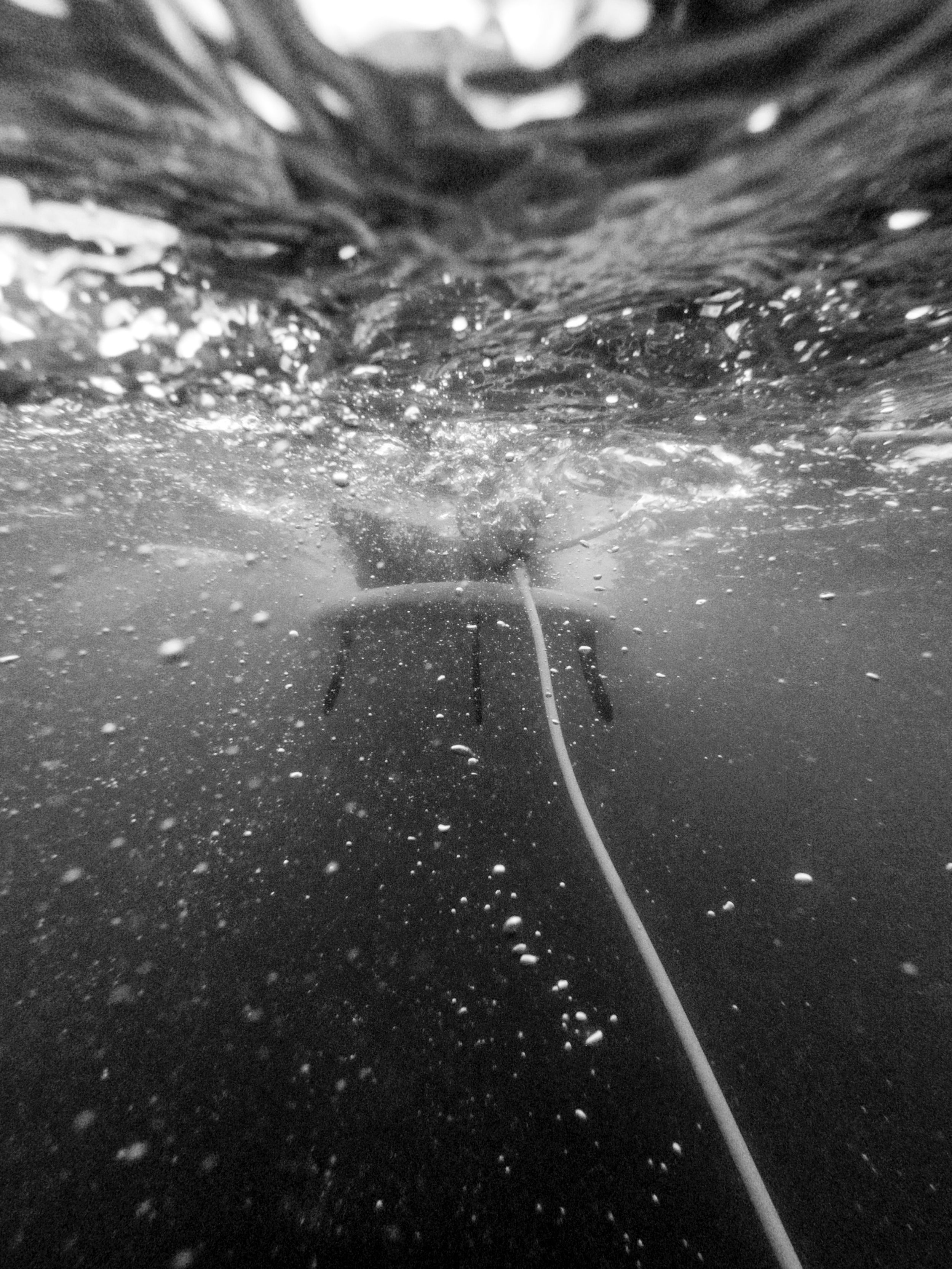 Underwater black and white photograph showing bubbles and light patterns beneath the surface.