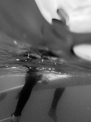 Black and white underwater view of legs breaking through the water's surface.