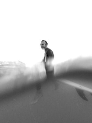 Artistic black and white underwater photo of a surfer silhouette emerging from waves.