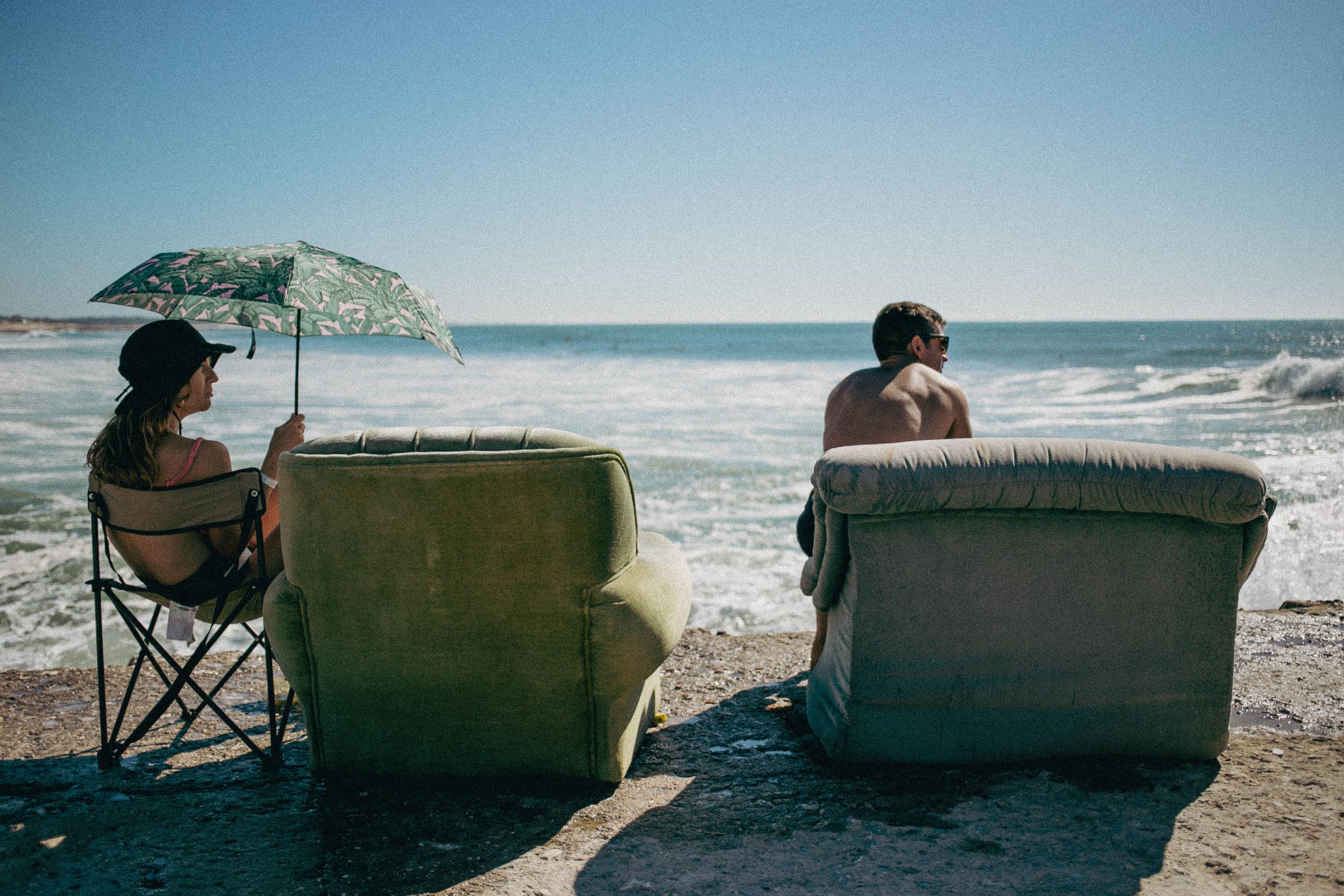 Two beach chairs facing the ocean waves under a bright blue sky.