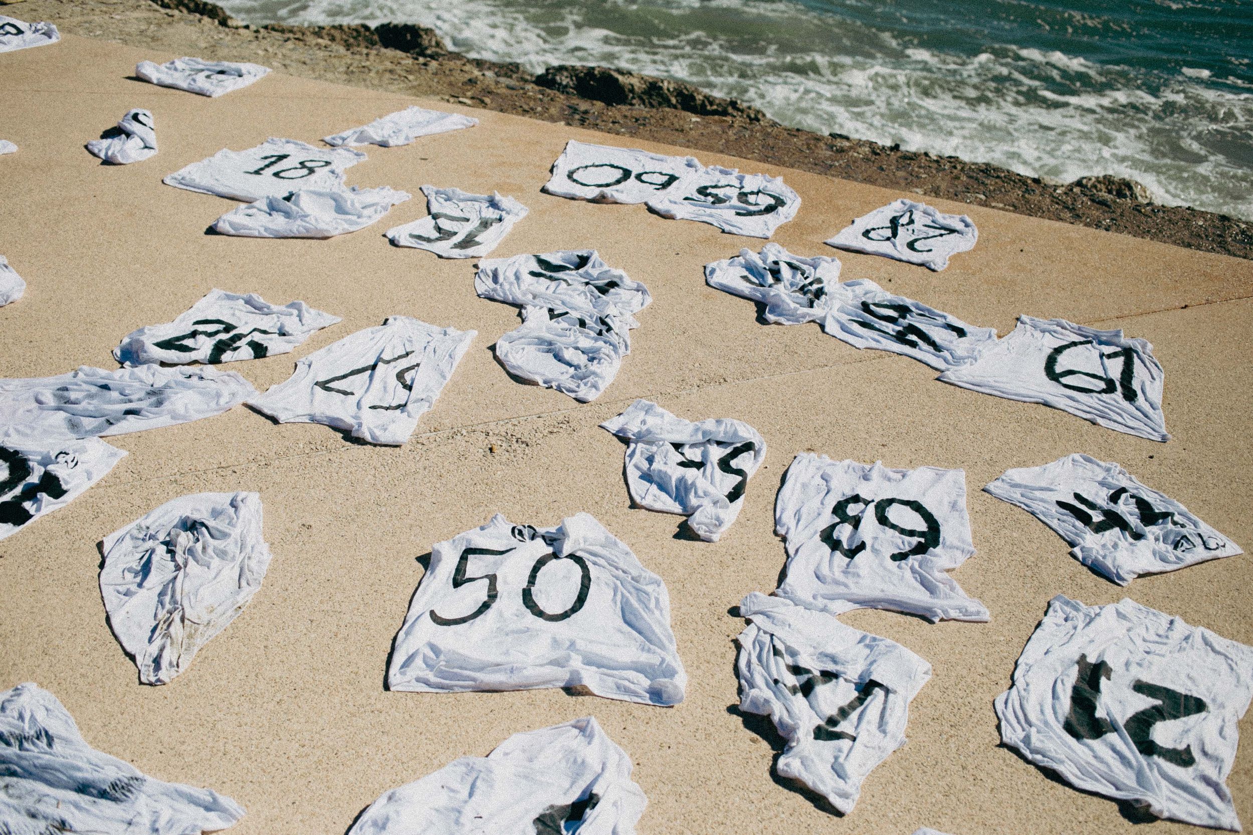 Numbers and symbols drawn on pieces of paper scattered across sandy beach.