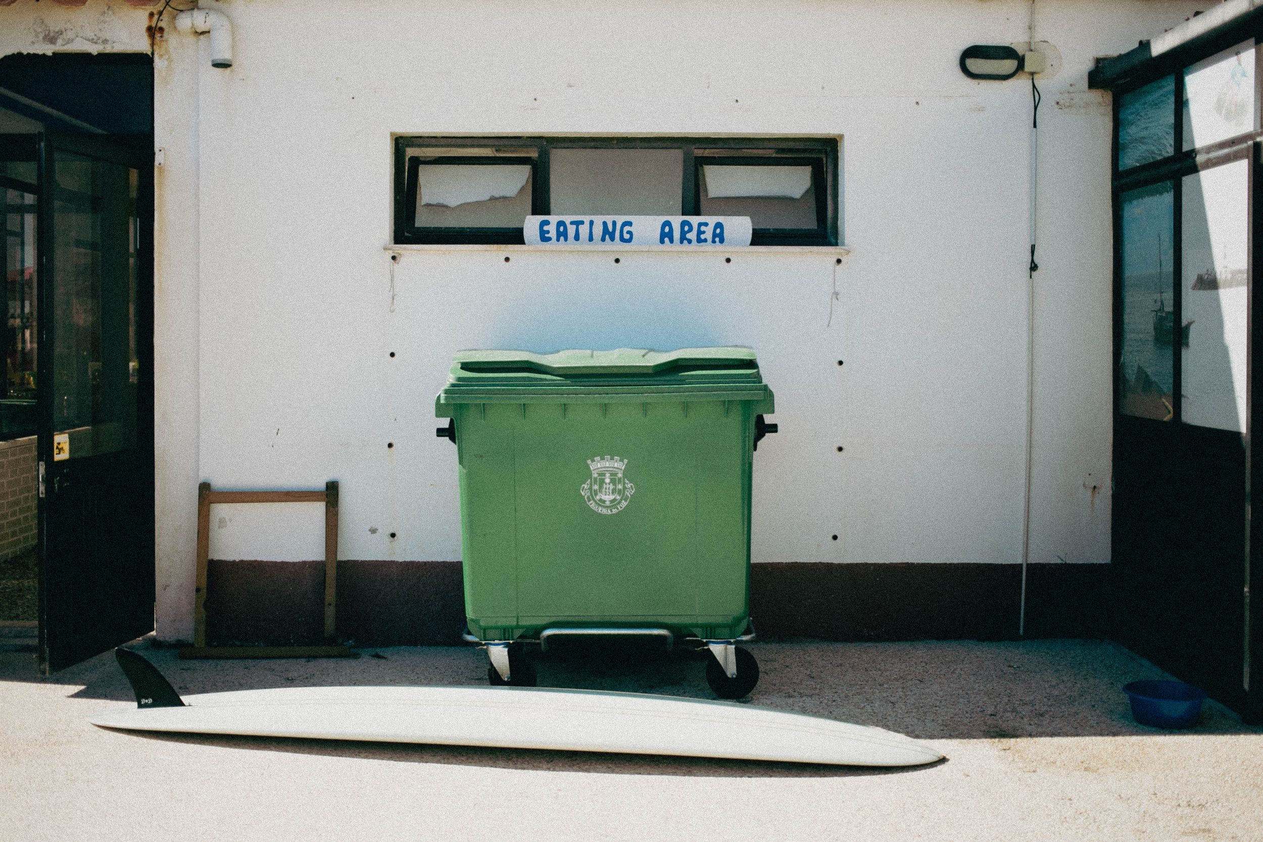Green industrial waste bin against white wall with small windows above.