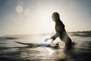 Silhouette of a surfer on a board at sunset with golden light reflection on water.