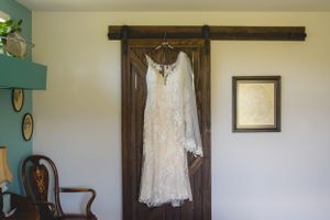 White lace wedding dress hanging on rustic barn door against light blue wall.