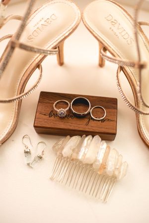 Wedding rings and accessories displayed on wooden blocks with elegant heels and a decorative hair comb.