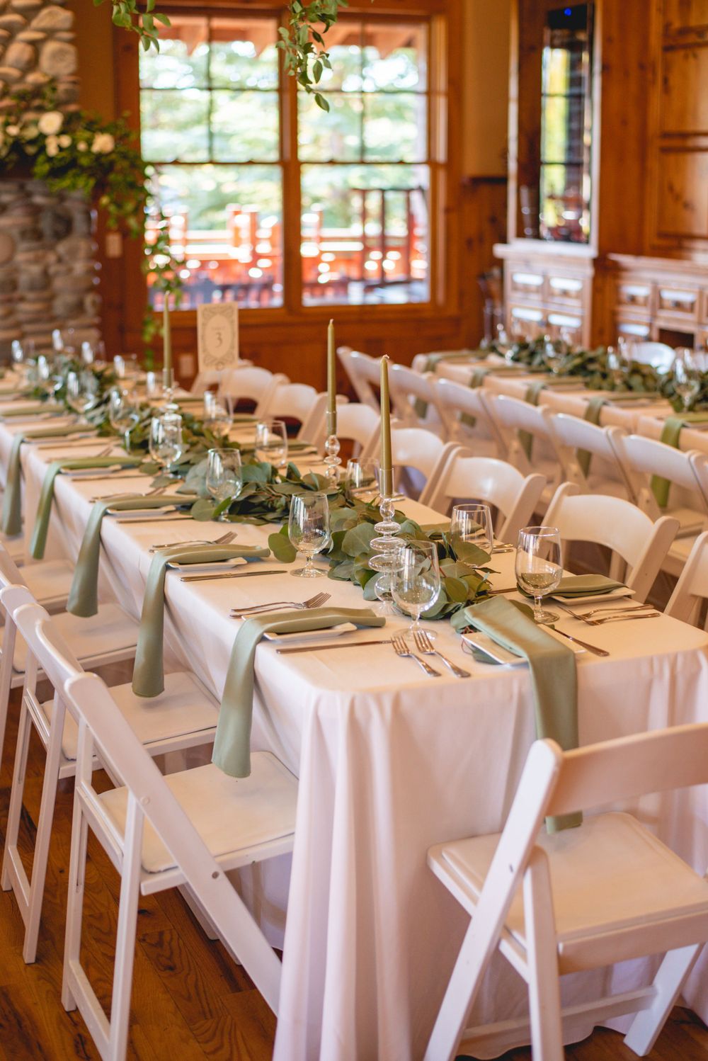 Elegant wedding reception table setting with white linens and greenery centerpieces.