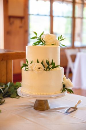 Two-tier white wedding cake decorated with fresh roses and greenery on wooden stand.