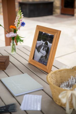 Guest book table at a wedding reception with natural wood frames and vases of wildflowers on a wooden surface.