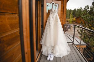 White wedding dress and shoes hang on wooden balcony with mountain forest view.