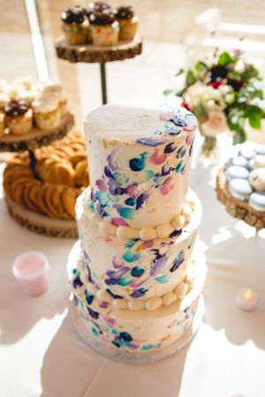 Three-tiered white wedding cake decorated with watercolor-style brushstrokes in blue and purple tones.