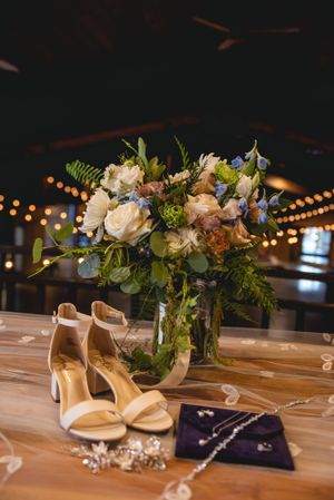 Elegant floral centerpiece with white roses alongside bridal shoes and jewelry.