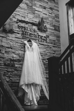 Wedding dress hanging against a stone wall with Spruce Mountain venue signage.