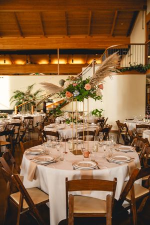 Elegant wedding reception venue with wooden beams and tables set with white linens and tall floral centerpieces.