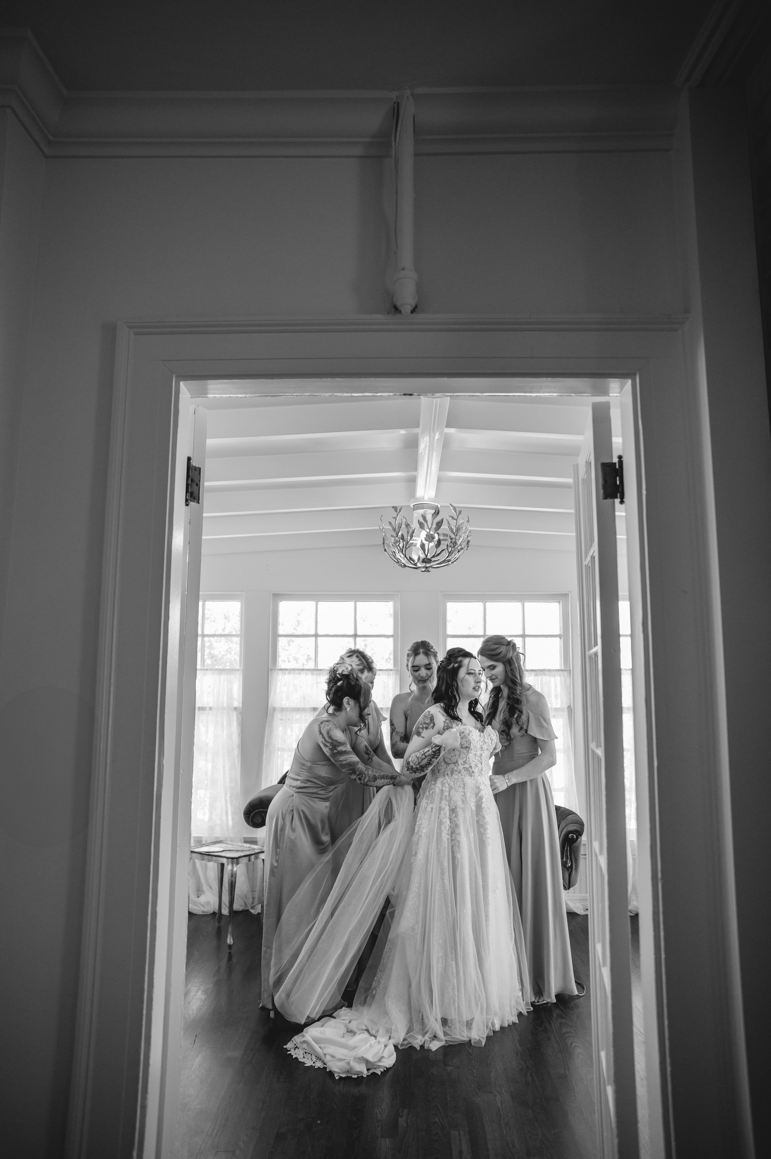 Black and white photo capturing preparations in an elegant room with natural window light.