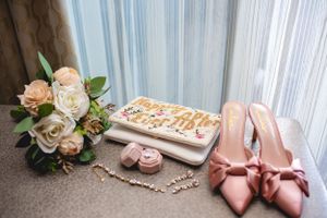 Bridal accessories including pink shoes, clutch, and rose bouquet arranged on carpet.