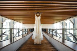 White wedding gown hanging in modern hallway with wooden ceiling and glass walls.