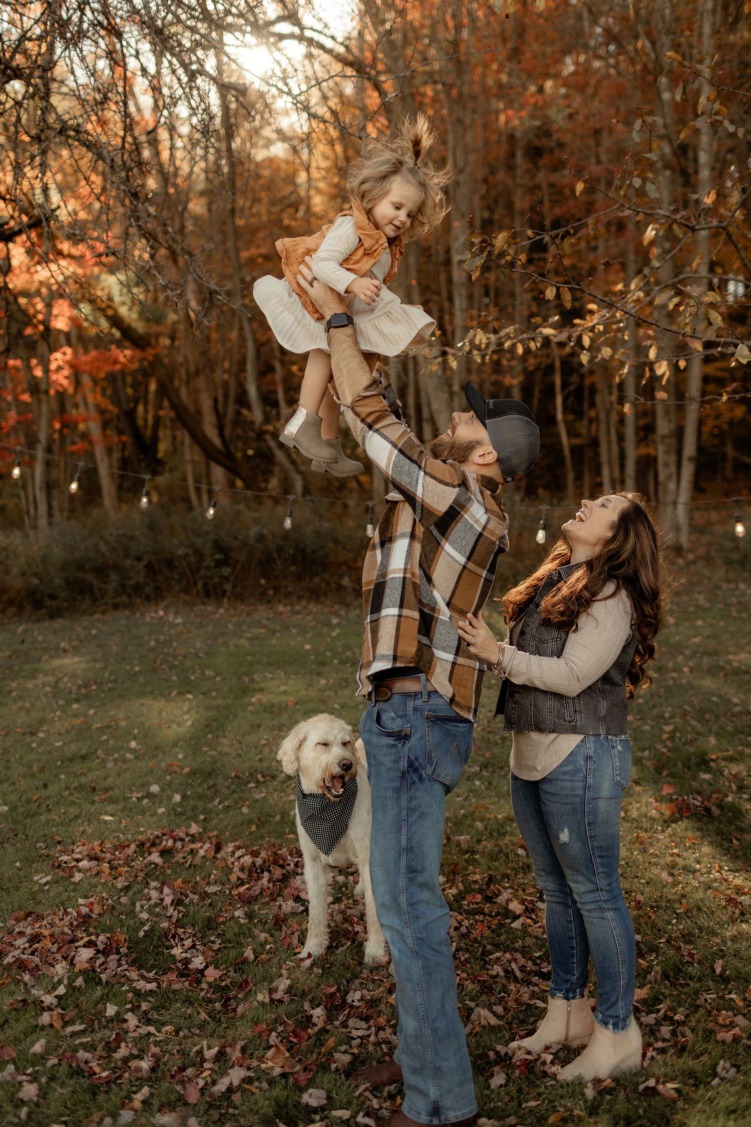 Couple in autumn attire holding hands while walking by lakeside during golden hour.