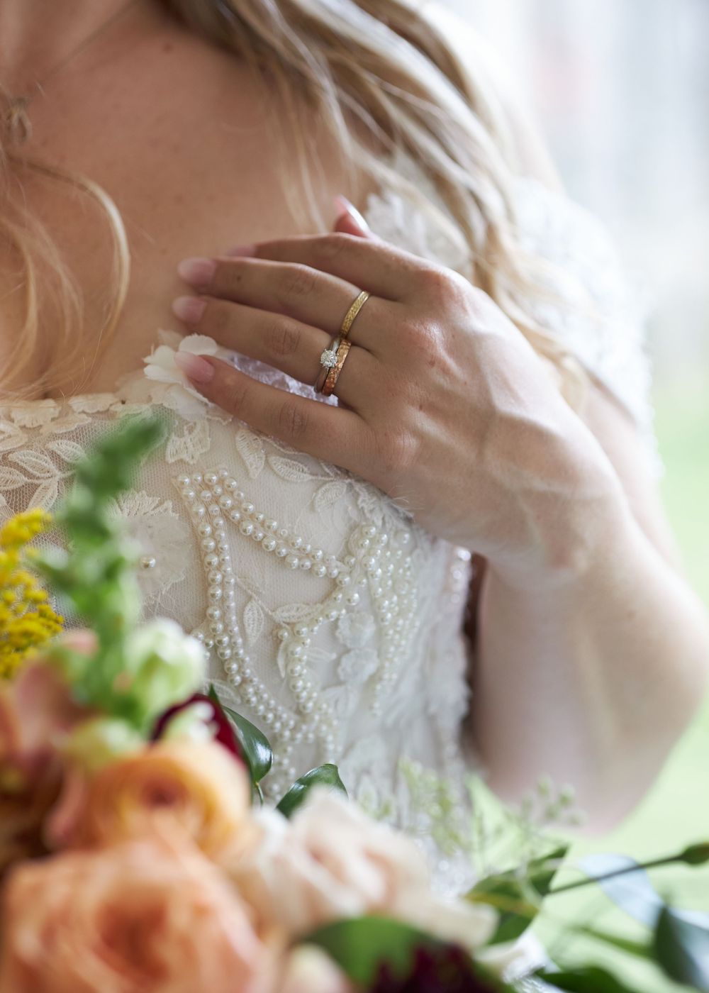 Close-up detail of a delicate lace wedding dress sleeve with pearl embellishments and a diamond ring.
