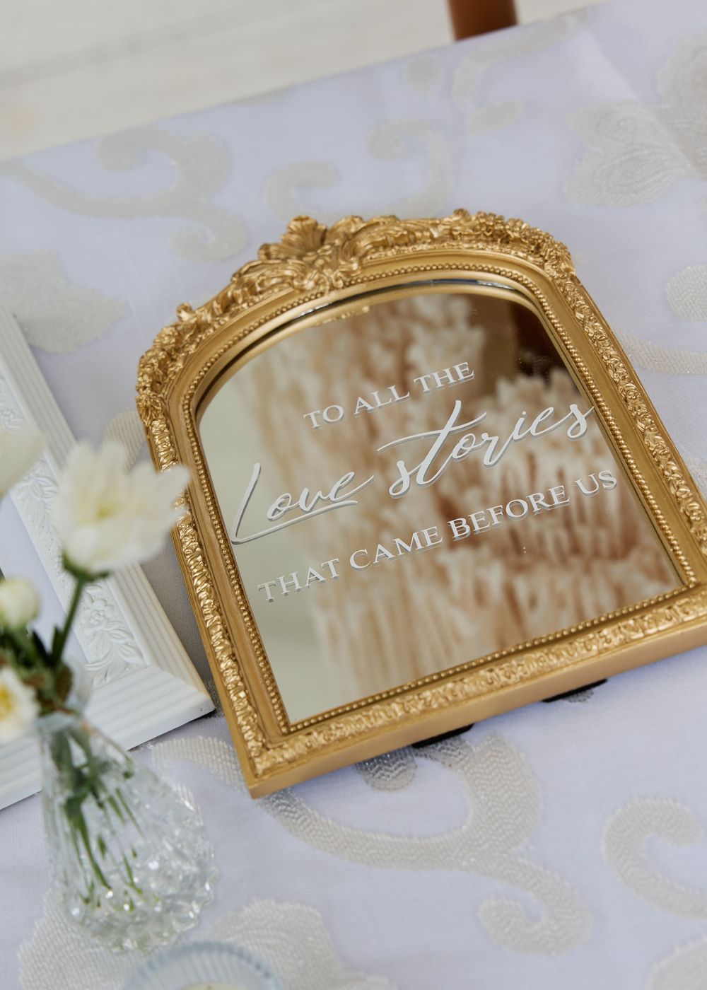 Gold ornate framed mirror with elegant wedding sign reading 'To All The Love Stories That Came Before Us'.