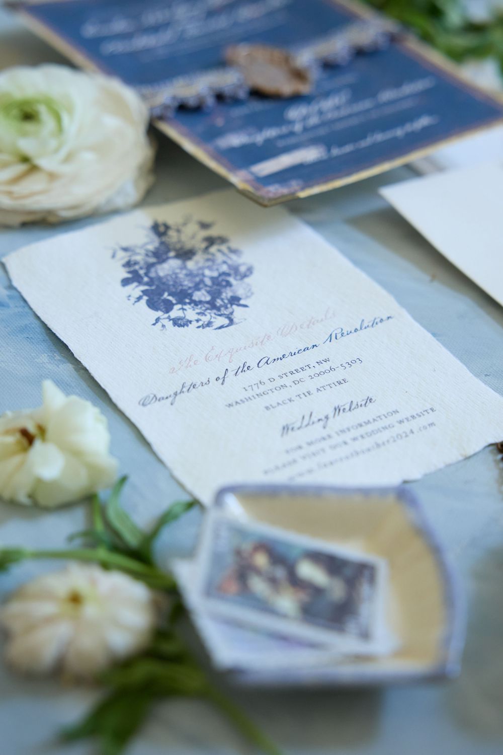 Elegant white and blue floral wedding invitation suite with cream roses and delicate details arranged on a light surface.
