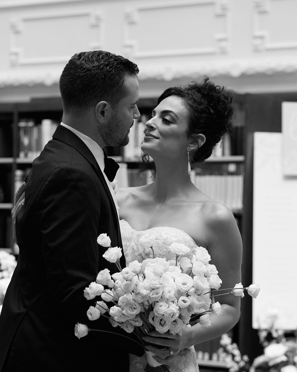 A romantic black and white wedding photo showing a couple sharing an intimate moment with a bouquet of white roses.