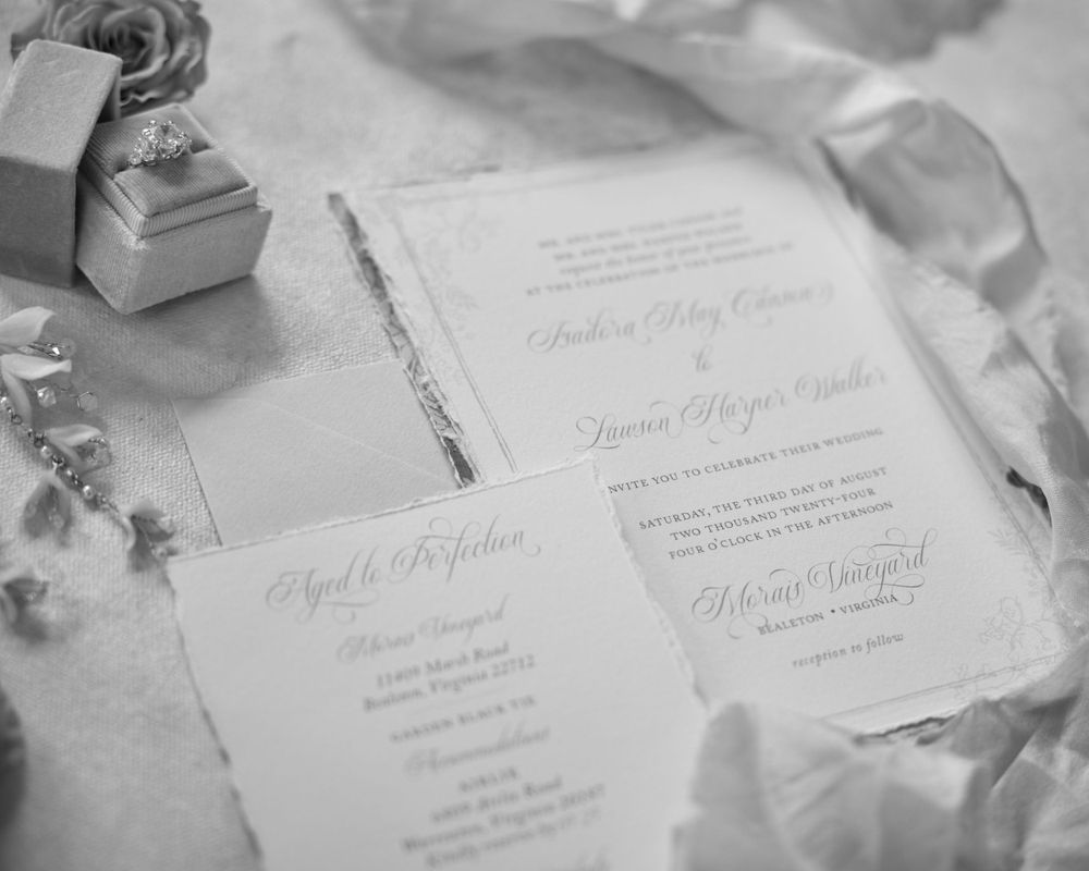 Elegant wedding invitations in black and white with calligraphy text laid out on silk fabric beside a ring box.