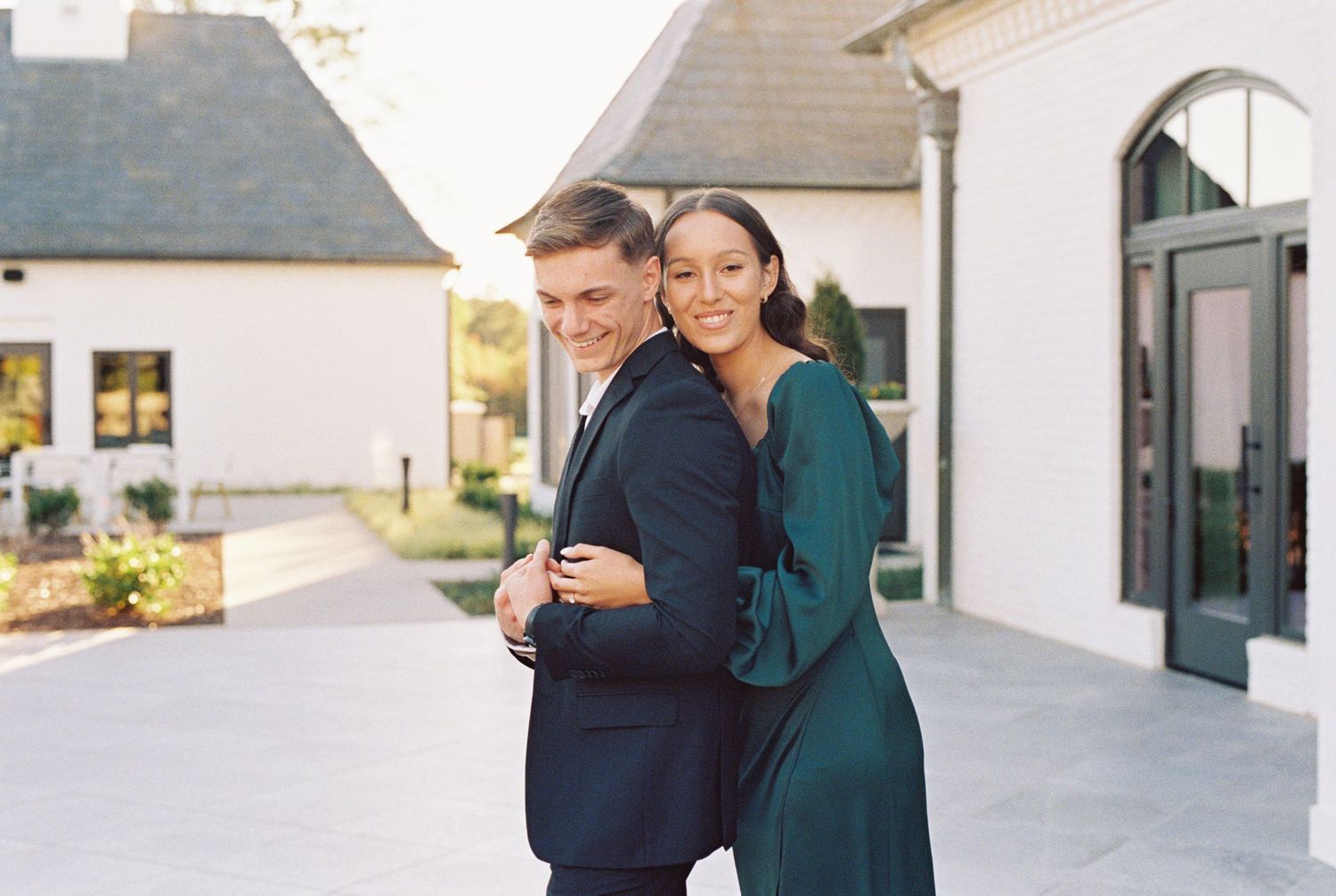 Couple in formal attire sharing an intimate moment outside elegant white buildings.