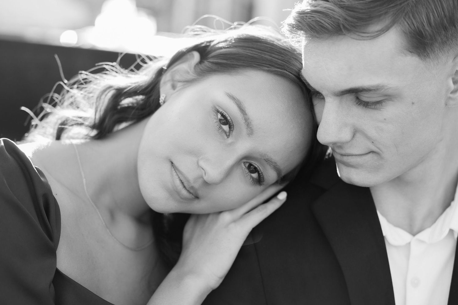Black and white intimate portrait of a couple in a tender moment, with her head resting near his shoulder.