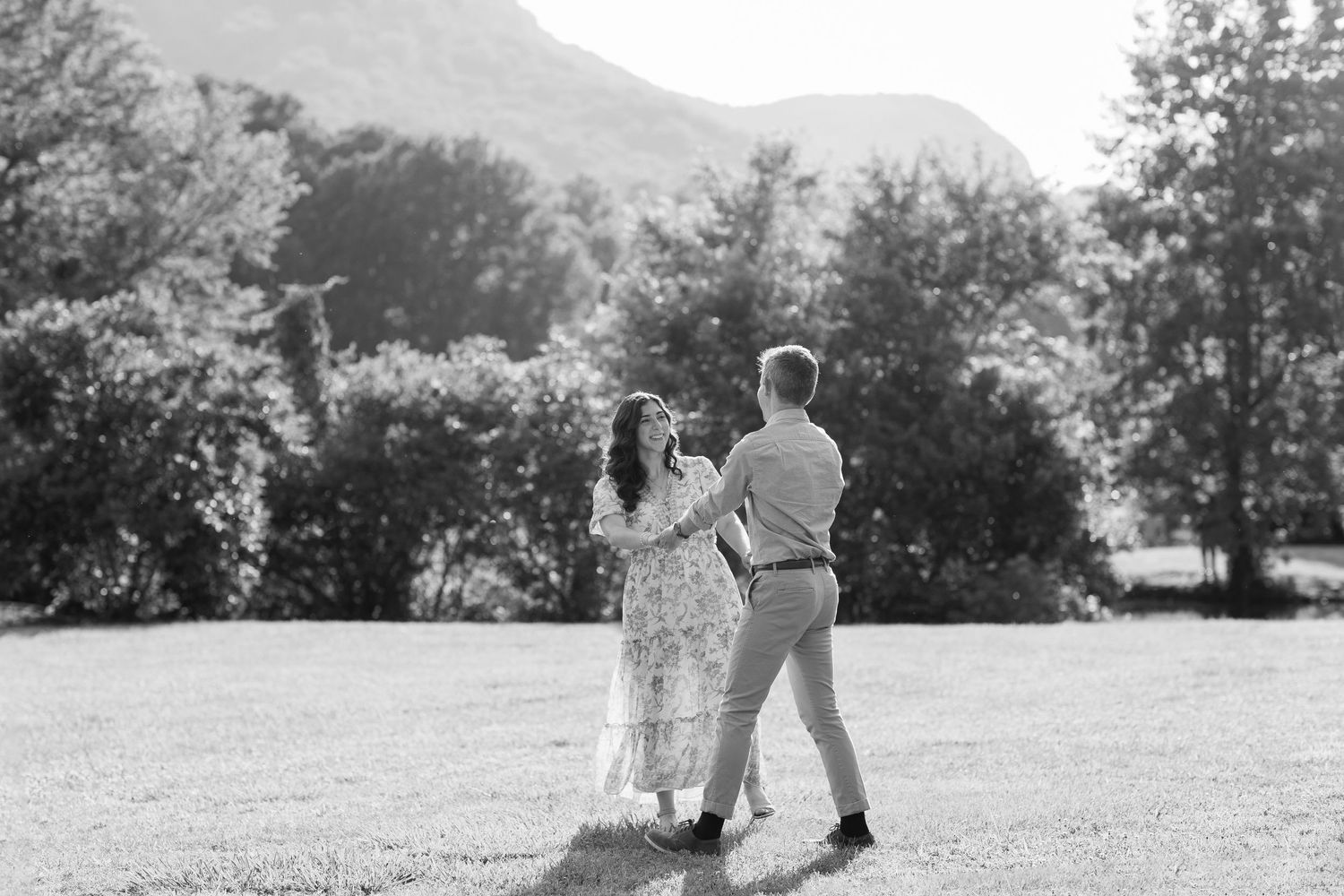 Couple dancing together in a sunlit meadow with mountains in the background.