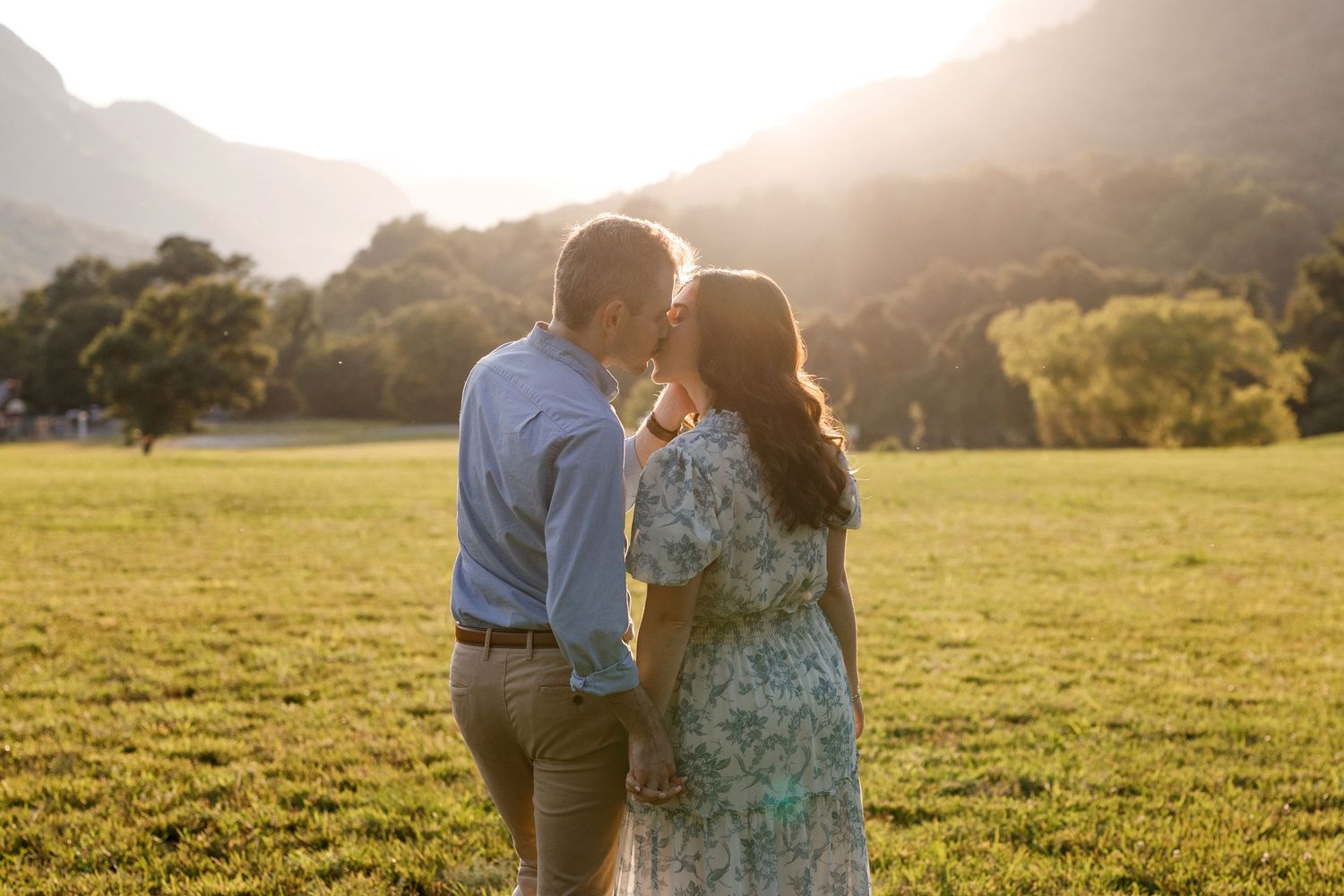 Romantic sunset portrait in meadow with mountains visible in background.