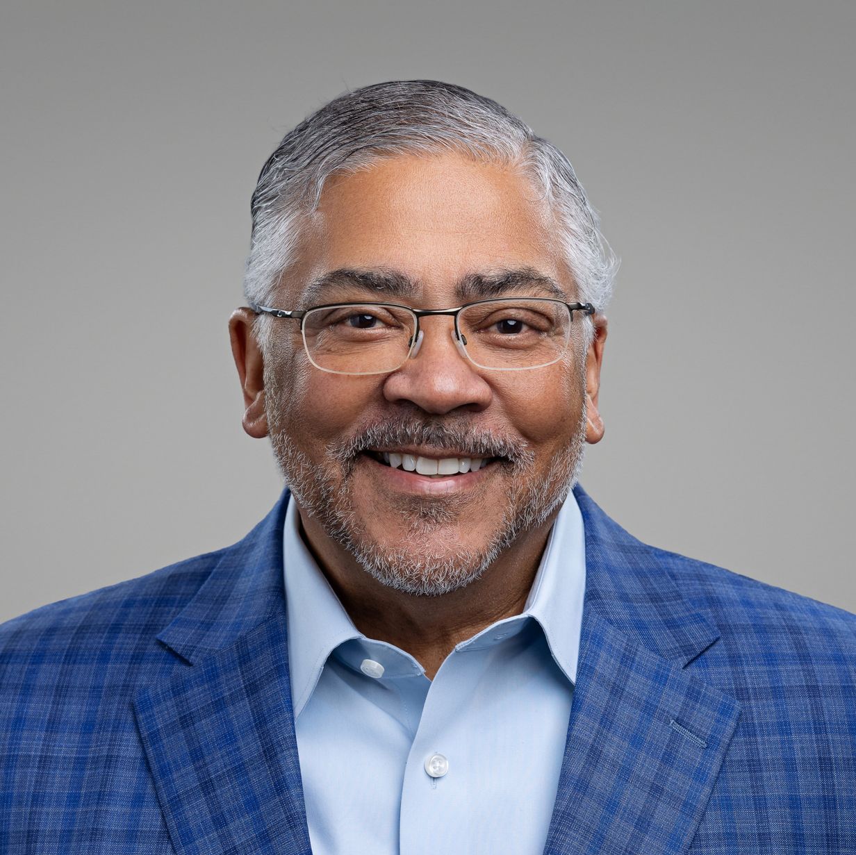 Clean professional headshot series against gray backdrop wearing checkered shirt.