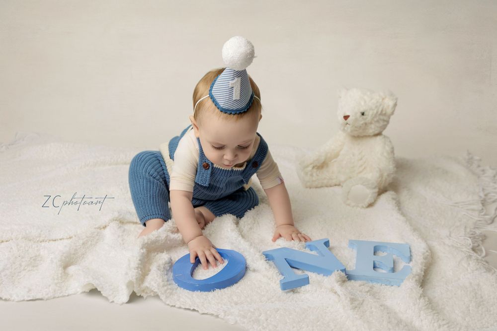 A baby wearing blue plays with paint on a light colored floor during a creative art activity.