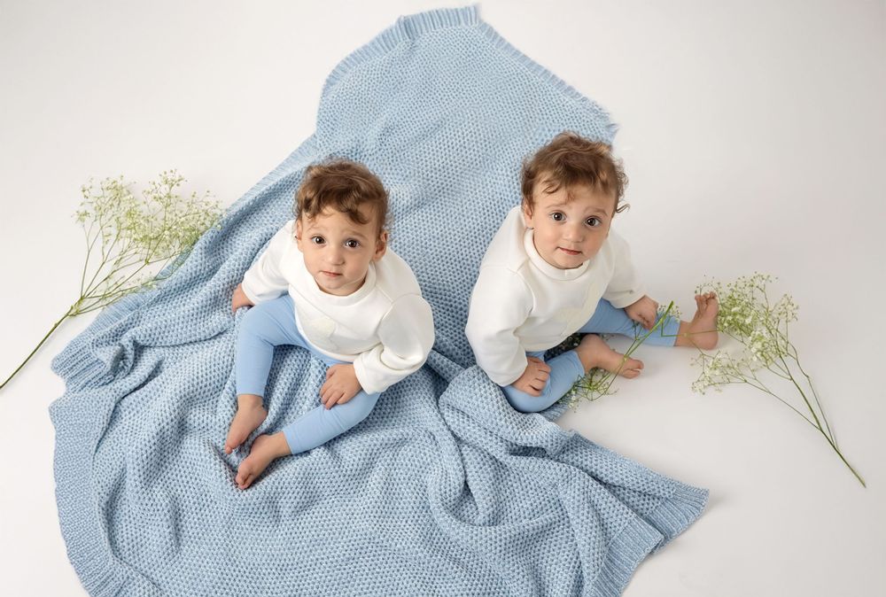Light blue baby swaddle blanket shown in multiple positions with delicate floral accents.