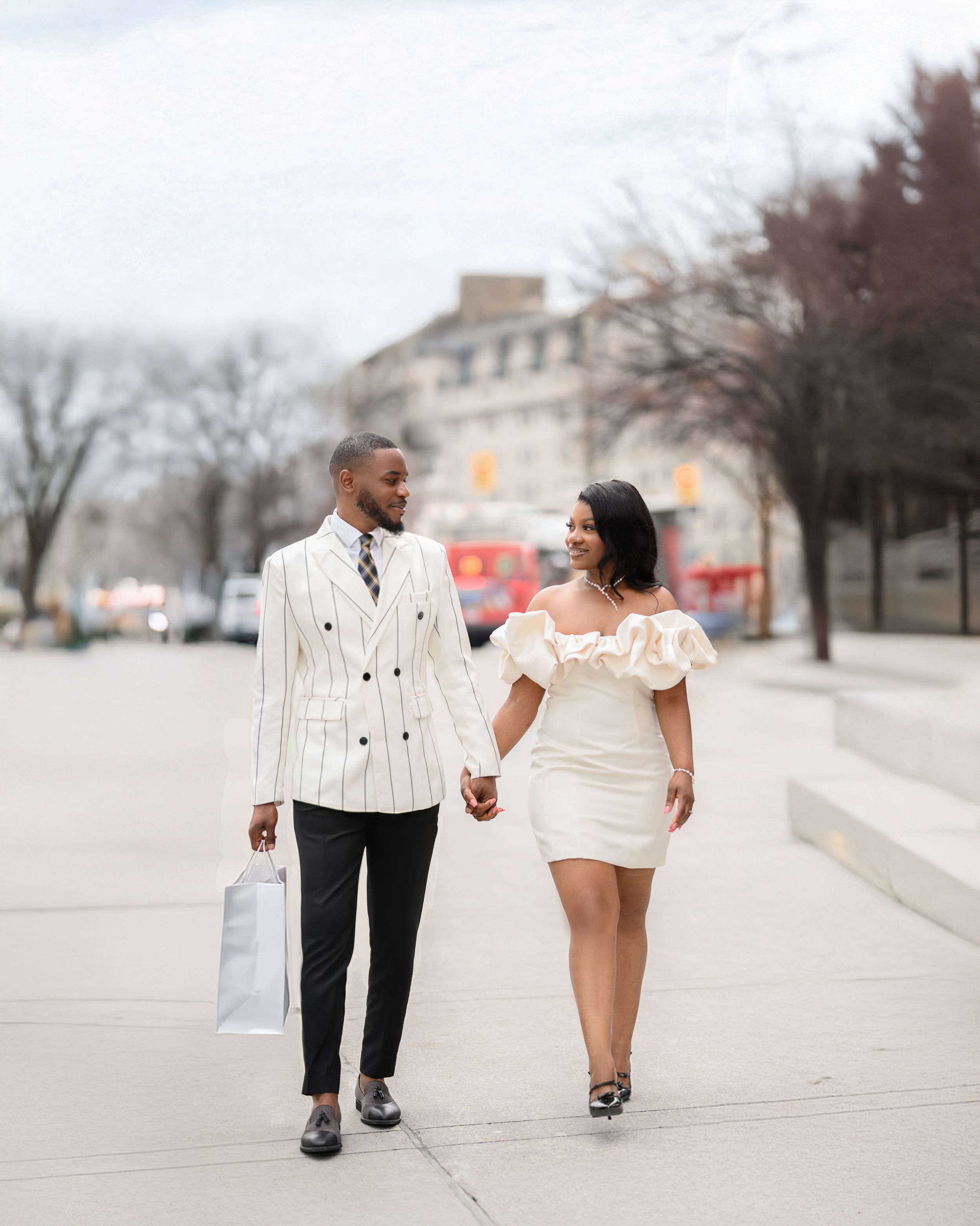 A couple walks hand in hand along a sidewalk on a winter day while bundled up in cozy outfits.