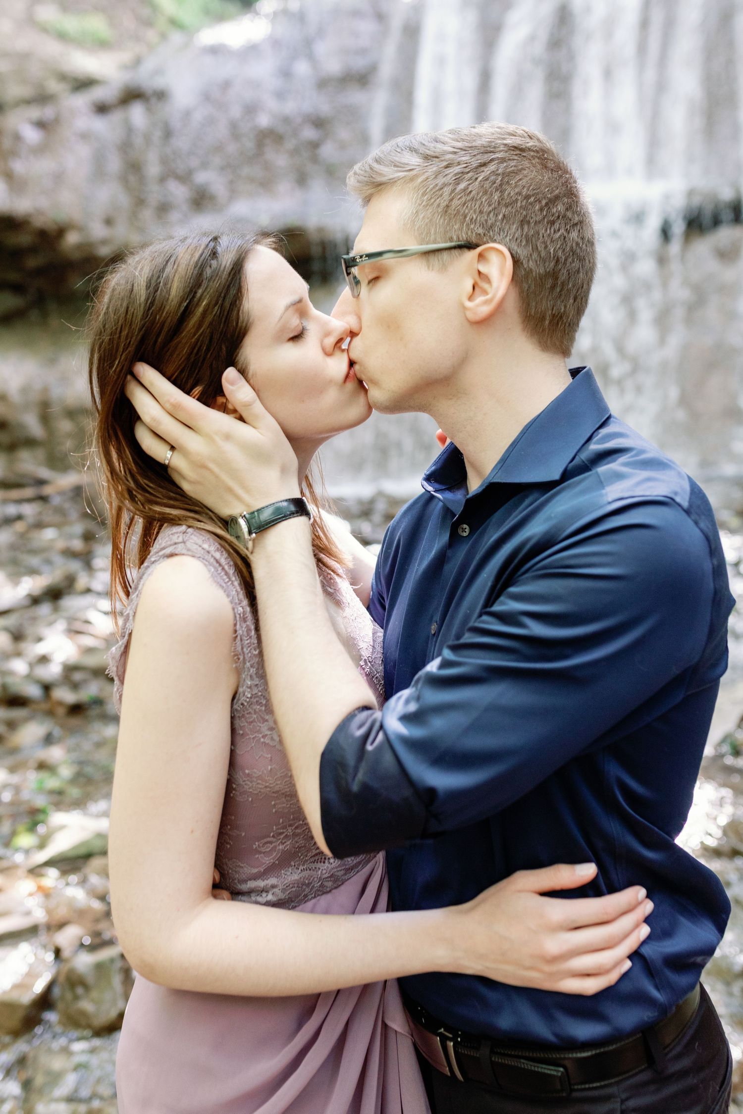Intimate moment shared between couple near a waterfall with rocks in background.