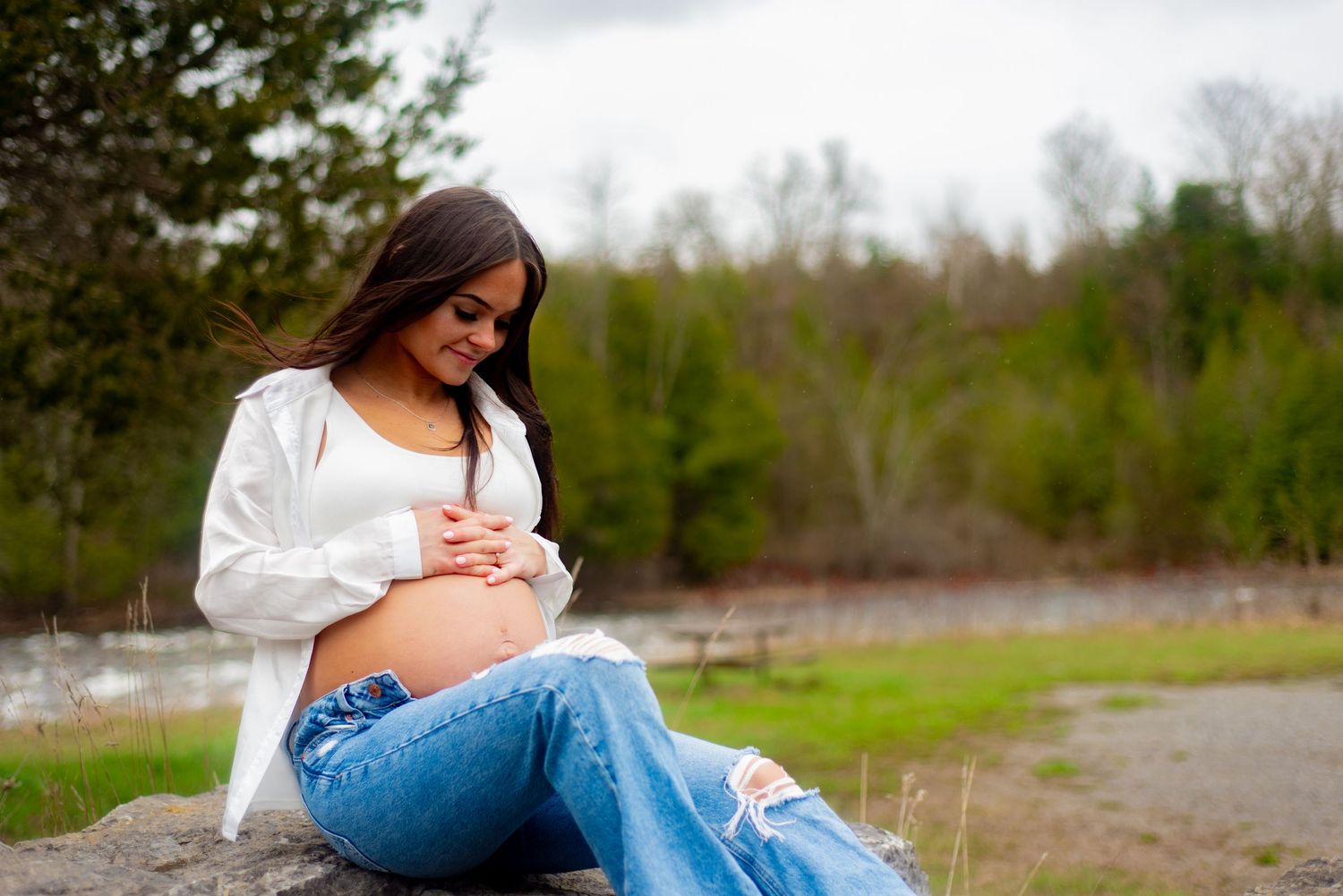 Candid moment of expectant mother sitting on rock during outdoor photography session.