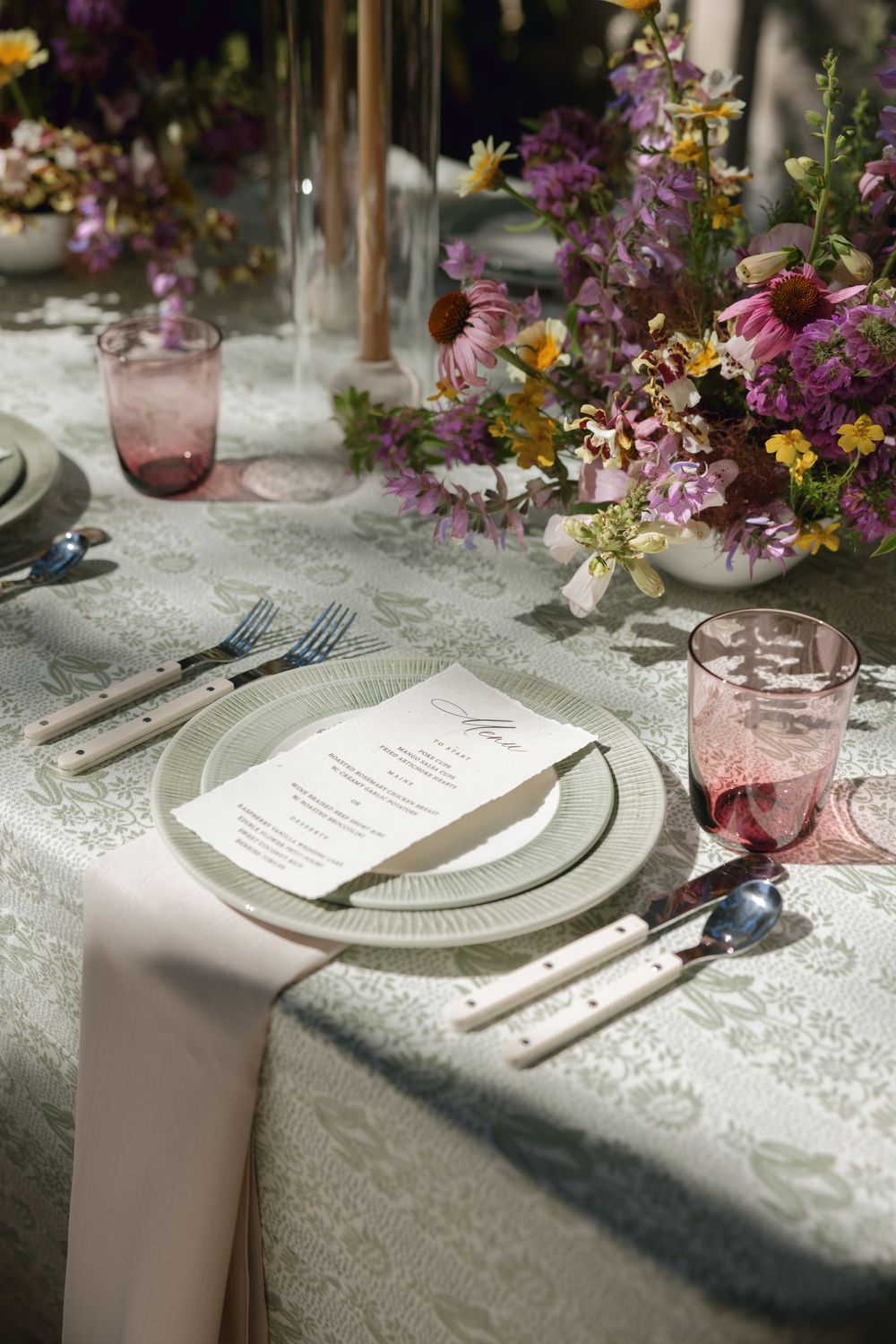 Elegant table setting with white lace tablecloth, purple glassware, and colorful floral arrangements for a special occasion.
