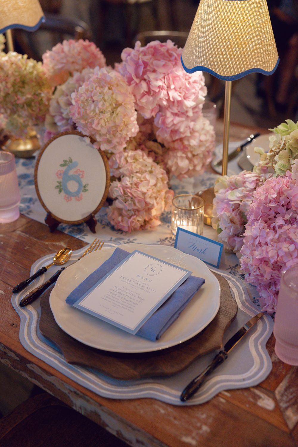 Elegant table setting with pink hydrangeas, blue and white plates, and gold table numbers for a wedding reception.
