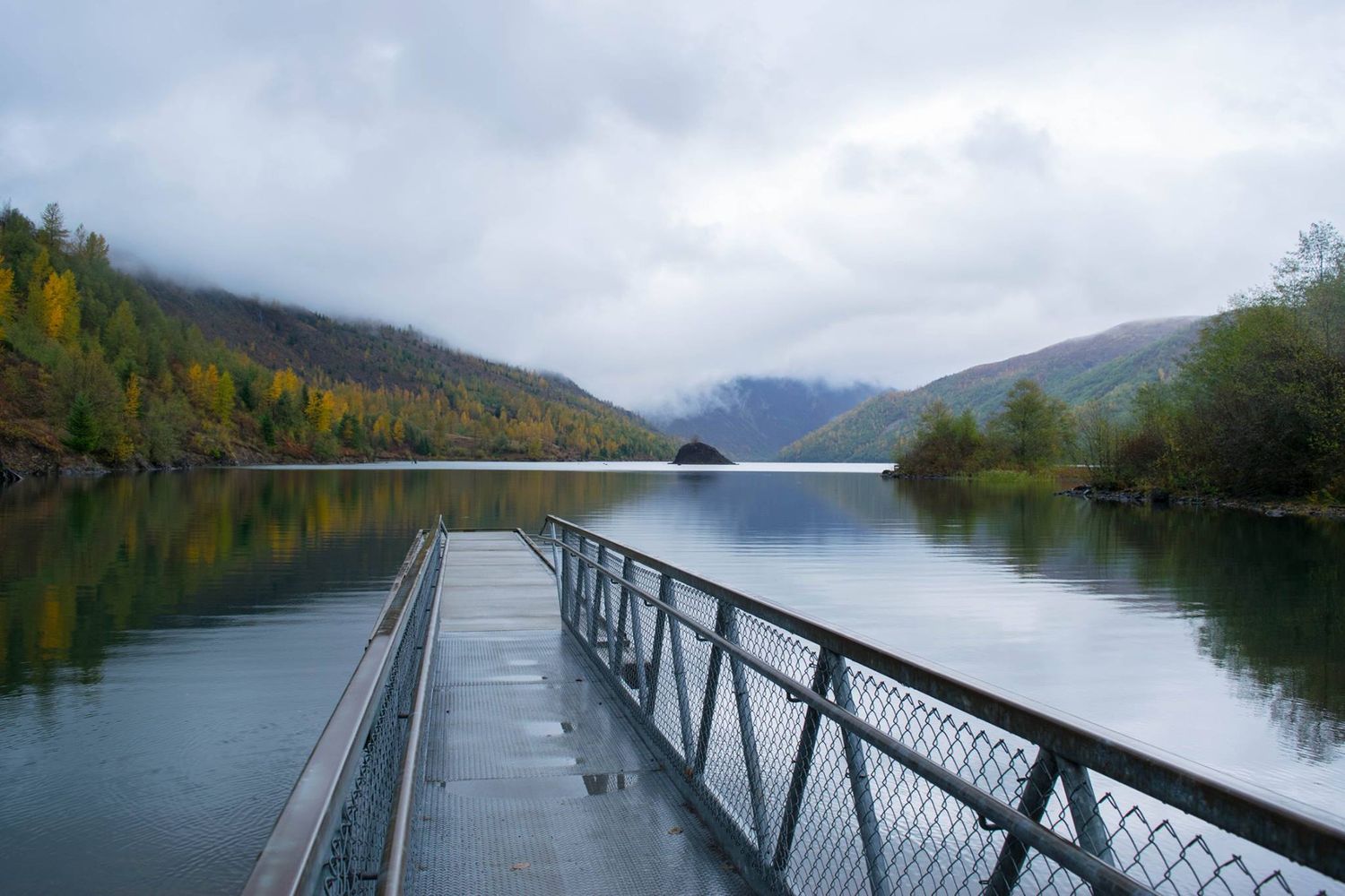 Metal dock extending into a misty mountain lake surrounded by fall foliage.