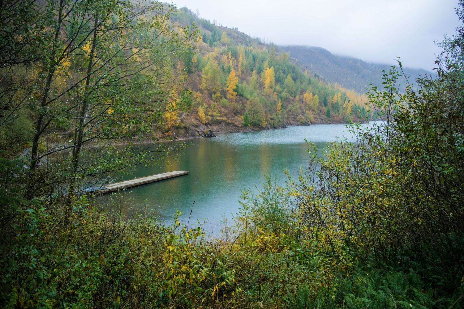 Scenic autumn lake view with colorful fall foliage and a wooden dock extending into calm waters.