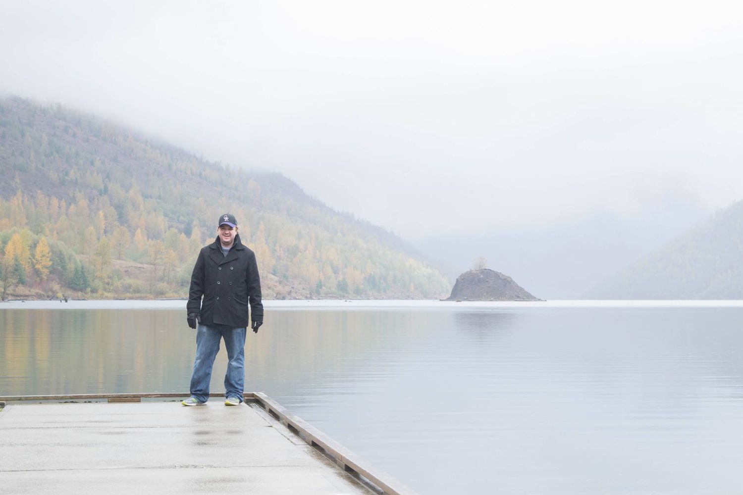 Figure stands on a foggy dock overlooking a peaceful mountain lake in autumn.