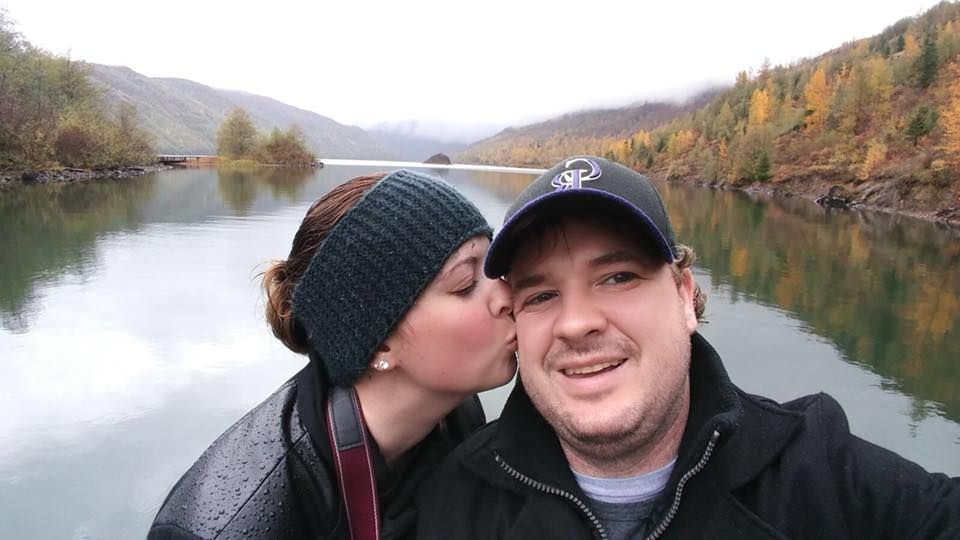 Couple takes selfie by scenic mountain lake surrounded by fall colors.