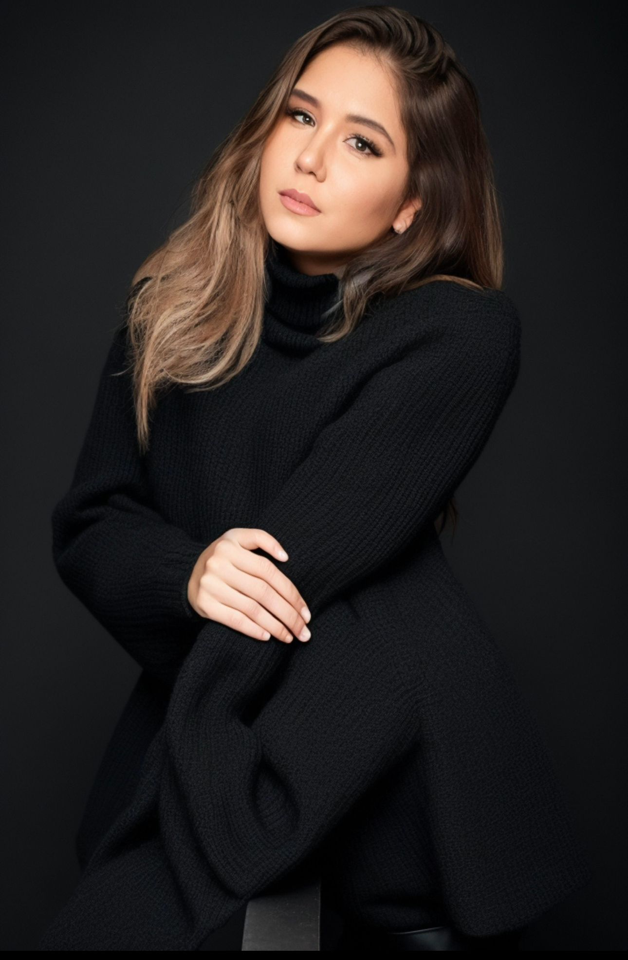 Studio fashion photo featuring a black knit sweater and long wavy hair against dark backdrop.