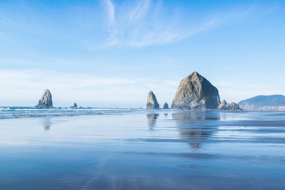 Haystack Rock formation at Cannon Beach reflecting in wet sand during low tide.