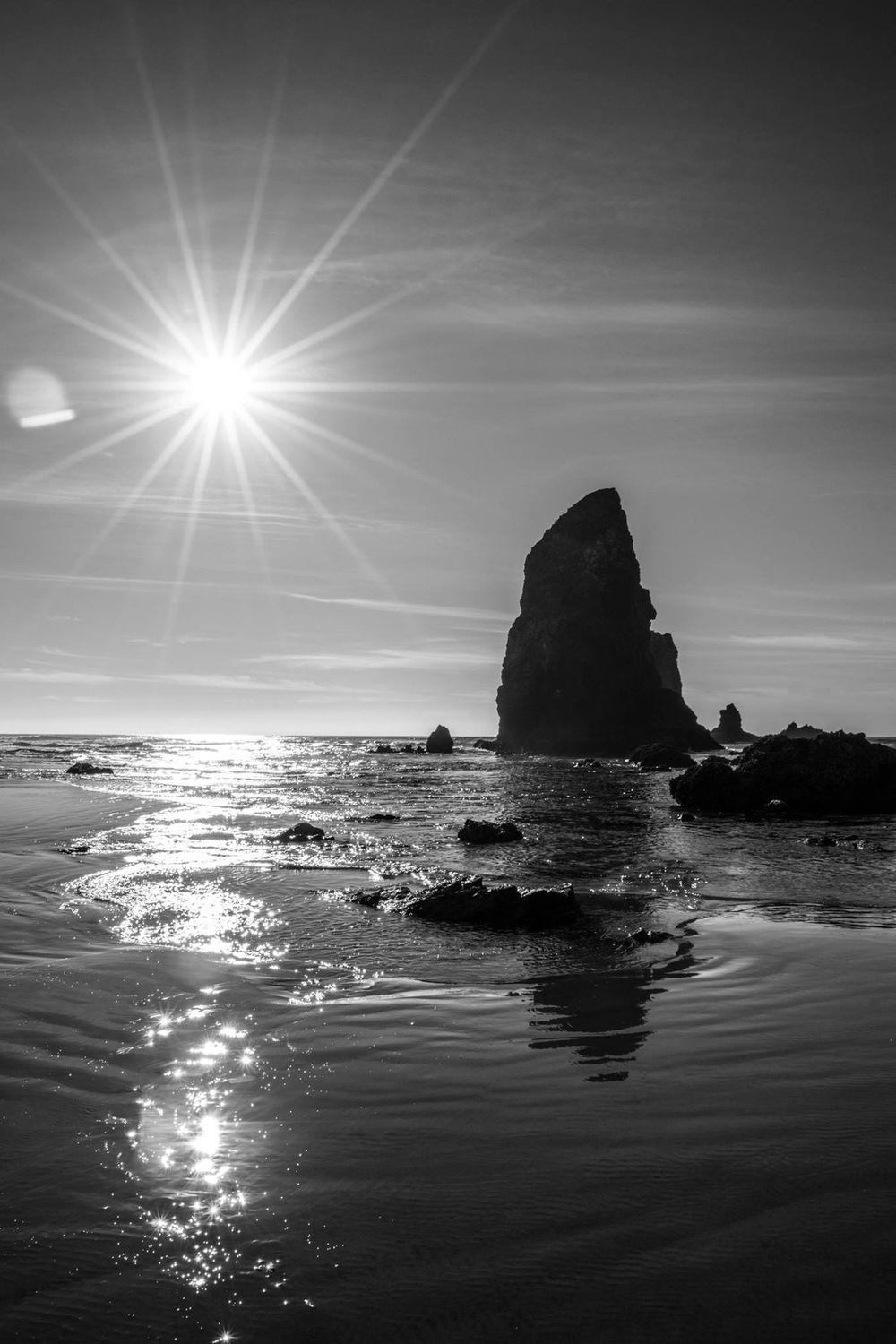 Dramatic black and white photo of sunburst over coastal rock formation.